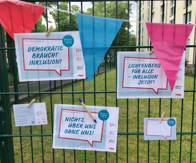 Forderungen des Aktionstages vom 5. Mai zu den Wahlen 2021 auf Papier gedruckt und mit Wimpelkette an der Zaun geklemmt.